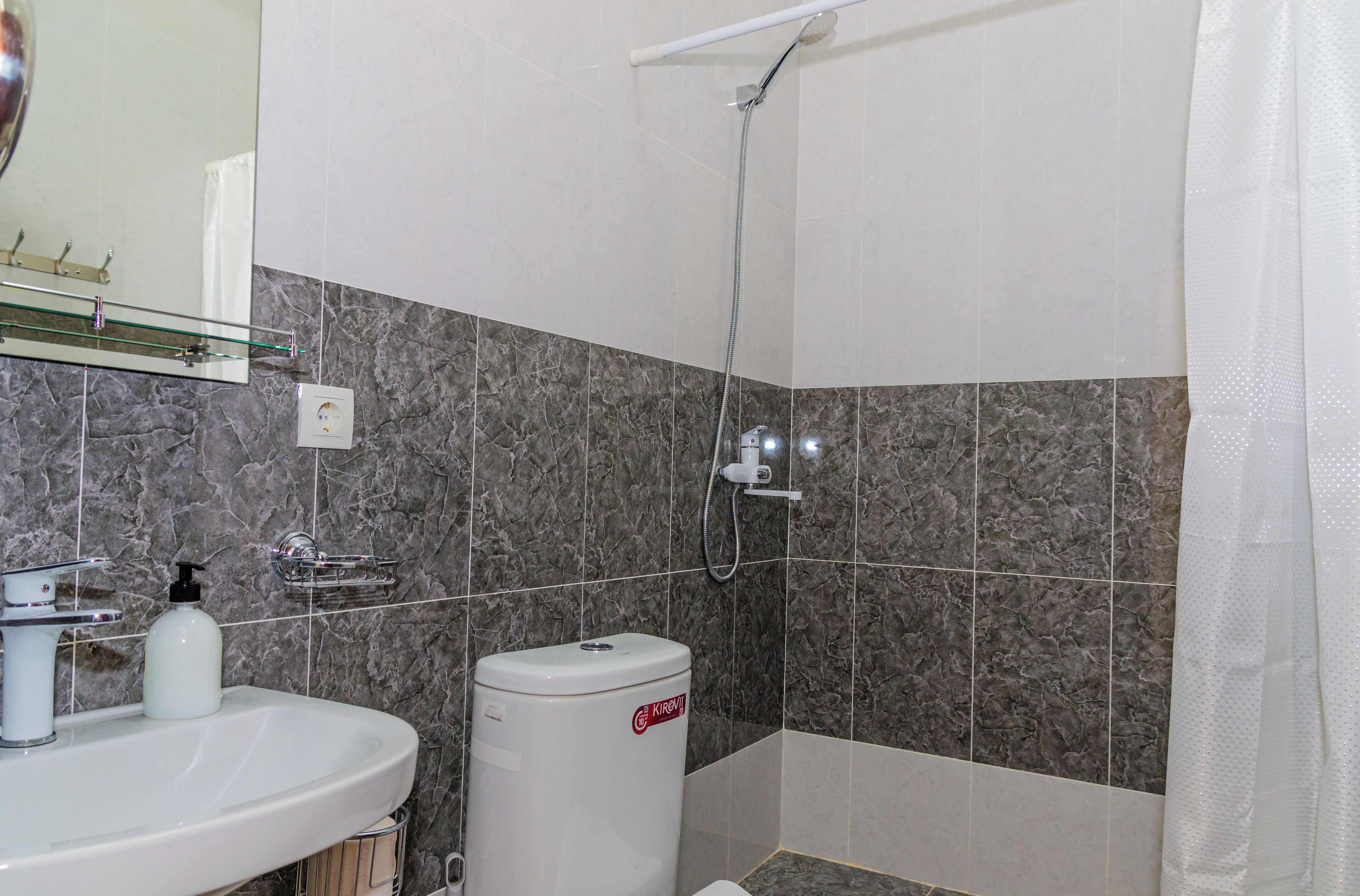 A bathroom with a sink, mirror, shower, and marble-tiled walls.