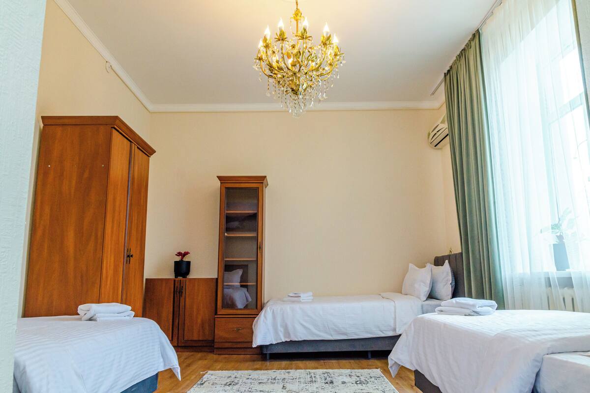 A hotel room with two beds, a wooden wardrobe, a tall cabinet, and a chandelier.