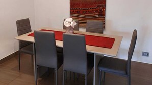 Ein moderner Essbereich mit einem langen Tisch, sechs Stühlen und einem dekorativen Wandteppich.
