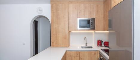 Una cocina moderna con armarios de madera, un microondas de acero inoxidable, un lavamanos y un hervidor rojo.