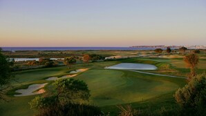 En golfbana med sandbunkrar, vattenhinder och utsikt över havet och den avlägsna stadsbilden.