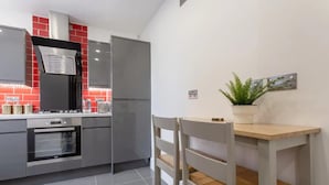 A modern kitchen with a built-in oven, a stainless steel refrigerator, and a red-tiled backsplash. There is a wooden dining table with chairs and a potted plant on the wall. - Gorgeous Duplex Near Canary Wharf, Excel & O2 (London)
