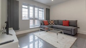 A modern living room with a grey sofa, a glass coffee table, and a remote control on a white console. - Gorgeous Duplex Near Canary Wharf, Excel & O2 (London)