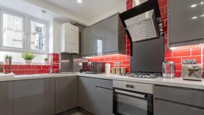A modern kitchen with grey cabinets, a red tiled backsplash, and stainless steel appliances including a stove and oven. - Gorgeous Duplex Near Canary Wharf, Excel & O2 (London)