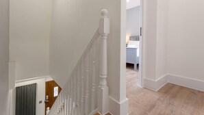 A staircase with white balusters leading to a bedroom with a bed and a nightstand. - Gorgeous Duplex Near Canary Wharf, Excel & O2 (London)