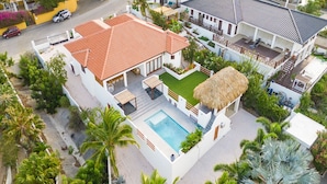 A white building with a red-tiled roof, a swimming pool, and a thatched-roof structure. - Villa Blou, steps from Jan Thiel Beach (Jan Thiel)