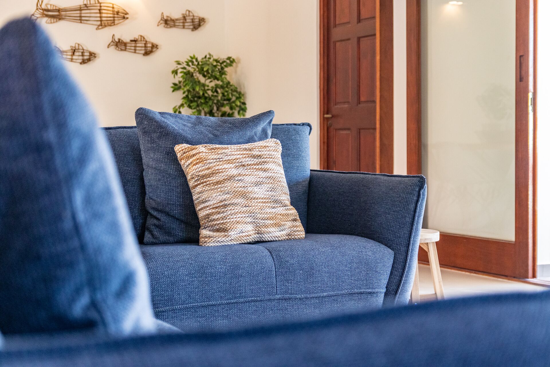 Un divano blu con un cuscino decorato e un piccolo sgabello in una stanza con una porta in legno e opere d'arte alle pareti.