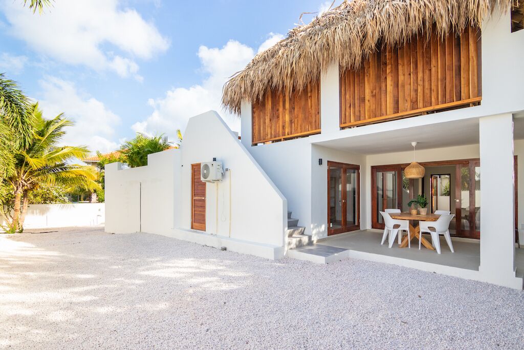 A two-story white building with a thatched roof, a covered outdoor seating area, and a gravel driveway.
