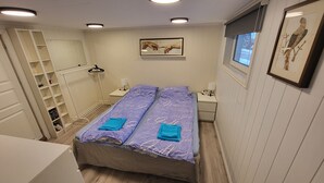 Ein Schlafzimmer mit einem Bett, einem Nachttisch, einer Hängelampe, einem Fenster mit Jalousien und einem gerahmten Bild an der Wand.