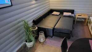 Ein gemütliches Zimmer mit einem Ecksofa, einem kleinen Tisch und einem an der Wand montierten Fernseher.