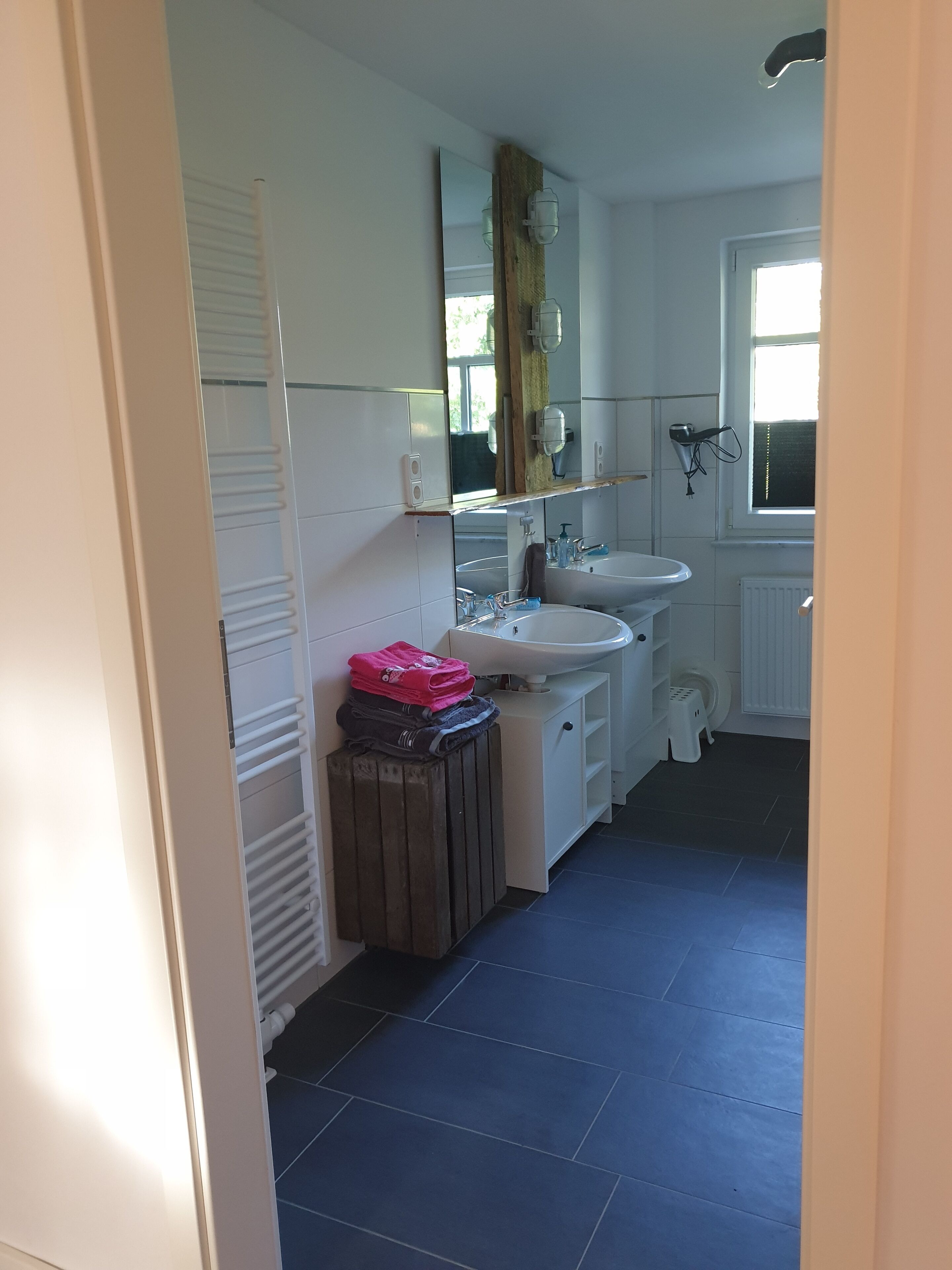 A bathroom with a white sink, mirror, and a radiator. There is a towel rack and a small stool.