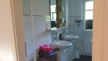 A bathroom with a white sink, mirror, and a radiator. There is a towel rack and a small stool.