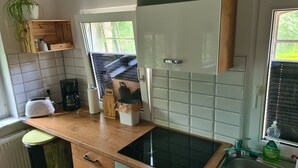 Eine Küche mit Holzarbeitsplatte, einem schwarzen Herd, einer Kaffeemaschine und einem Fenster mit Jalousien.