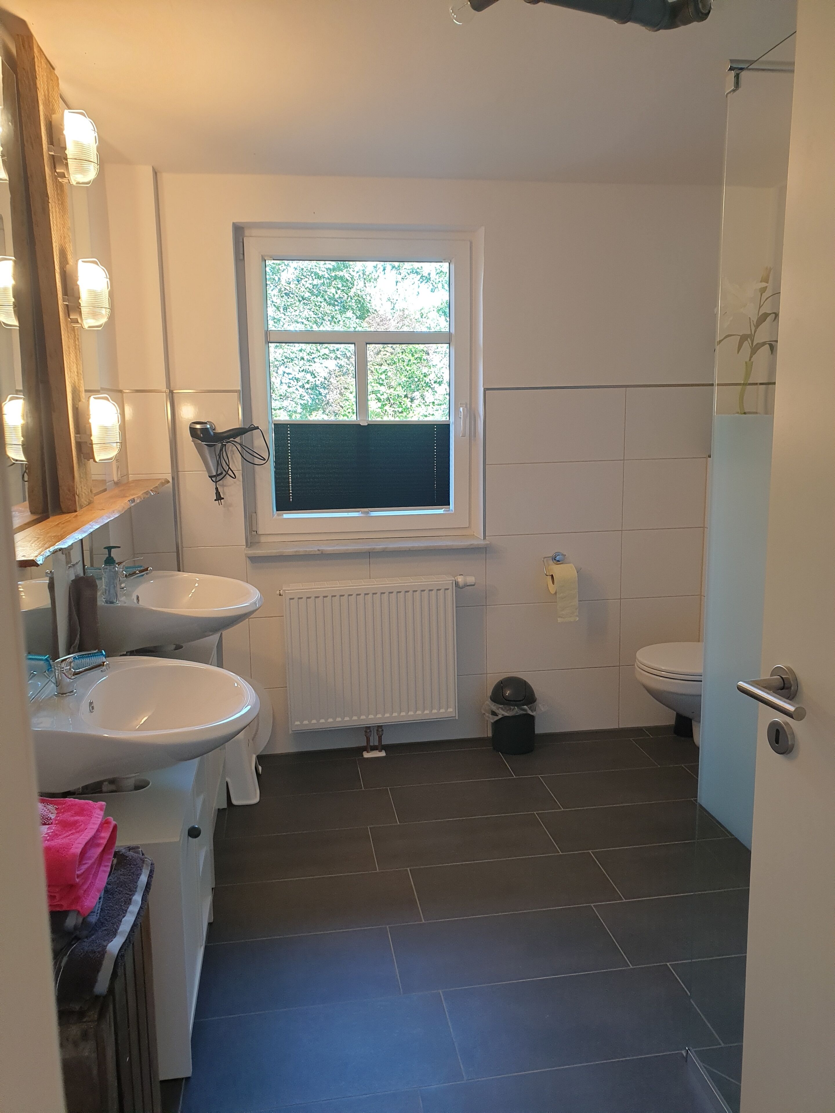 A bathroom with two sinks, a window, a toilet, and a shower.
