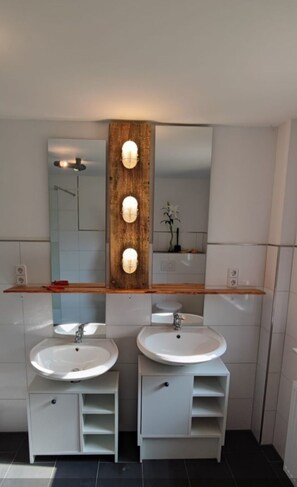 Een moderne badkamer met twee wastafels, een houten accentmuur en een grote spiegel.