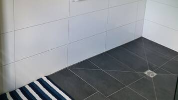 Ein Badezimmer mit Dusche, Haltegriffen und einer Streifen-Teppich.