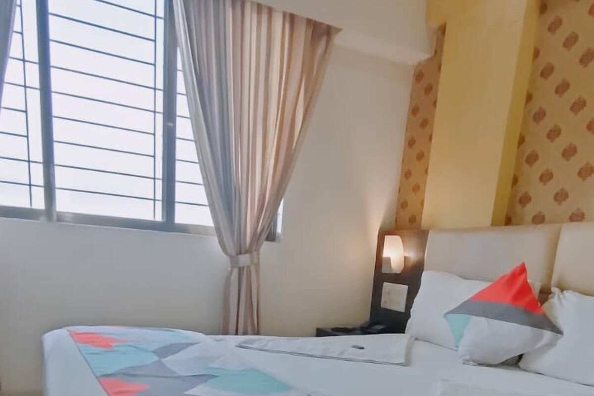 A hotel room with a bed, curtains, a nightstand, and a window with blinds.