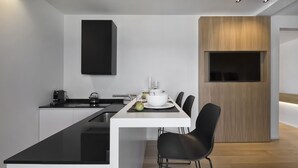 Une cuisine moderne avec un plan de travail blanc, des chaises noires et un mur d’accent en bois.