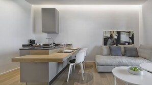 Une cuisine moderne avec un plan de travail en bois et des chaises blanches, un canapé gris agrémenté de coussins, et une table blanche sur laquelle se trouve un saladier rempli de pommes.