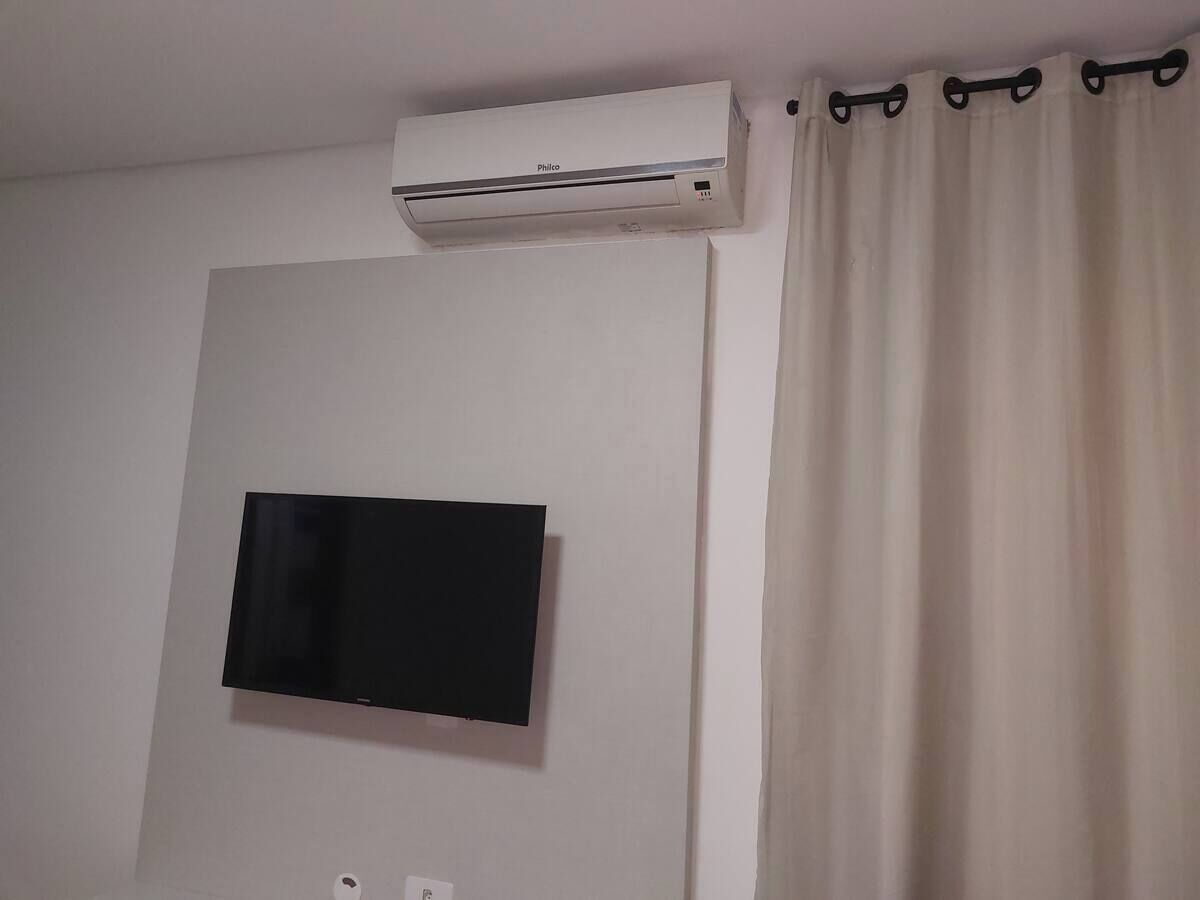 Een kamer met een wandgemonteerde flatscreen-tv, een airconditioning en een gordijn.