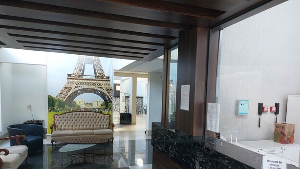 A lobby with a large mural of the Eiffel Tower, a plush sofa, a glass coffee table, and a reception desk with a wine box.
