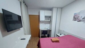 A hotel room with a bed, a desk, a chair, a television, and a small cabinet.