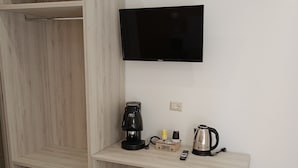 A modern room with a wooden wardrobe, a desk with a coffee maker, a kettle, and a flat-screen TV.