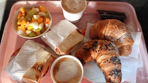 A tray with a sandwich, croissant, fruit salad, and two cups of coffee.