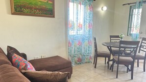 Un salon avec un canapé marron, des coussins colorés, une table à manger avec des chaises et un tableau accroché au mur.