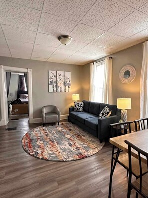 A living room with a sofa, armchairs, a coffee table, and a rug. There are two wall-mounted lamps and a ceiling light. - Urban Escape: Stylish Studio-Downtown Indianapolis- Unit 3 (Indianapolis)