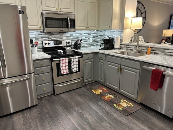 A modern kitchen with stainless steel appliances, a tiled backsplash, and a wooden floor. - Georgia Dawg House! Game weekend, business travel, this condo has it all! (Athens)