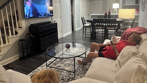 A living room with a TV, a glass coffee table, a sofa, and a dining area with chairs and a table. - Georgia Dawg House! Game weekend, business travel, this condo has it all!  (Athens)