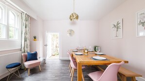 Ein Essbereich mit einem Holztisch, gedeckt für sechs Personen, rosa Stühlen und Blick auf den Garten durch eine offene Tür.