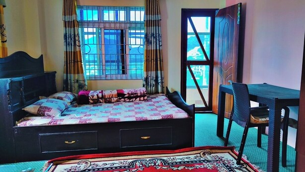 Une chambre à coucher avec un lit, un bureau et une chaise. Il y a une fenêtre avec des barreaux et des rideaux.