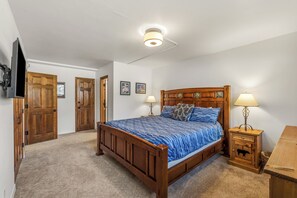 A bedroom with a wooden bed, two bedside lamps, a TV mounted on the wall, and a wooden cabinet. - Phoenix 2-Bedroom Condo – Comfort, Convenience, and Steps from the Slopes! (Steamboat Springs)