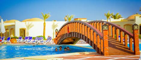 A pool area with a brick arch bridge, lounge chairs, and palm trees.