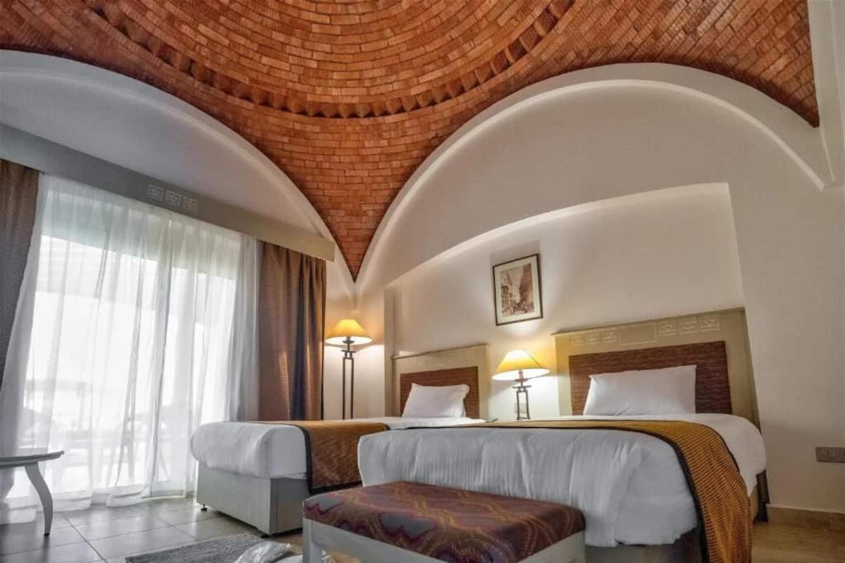 Une chambre d’hôtel avec deux lits, un plafond en briques et une grande fenêtre avec des rideaux.