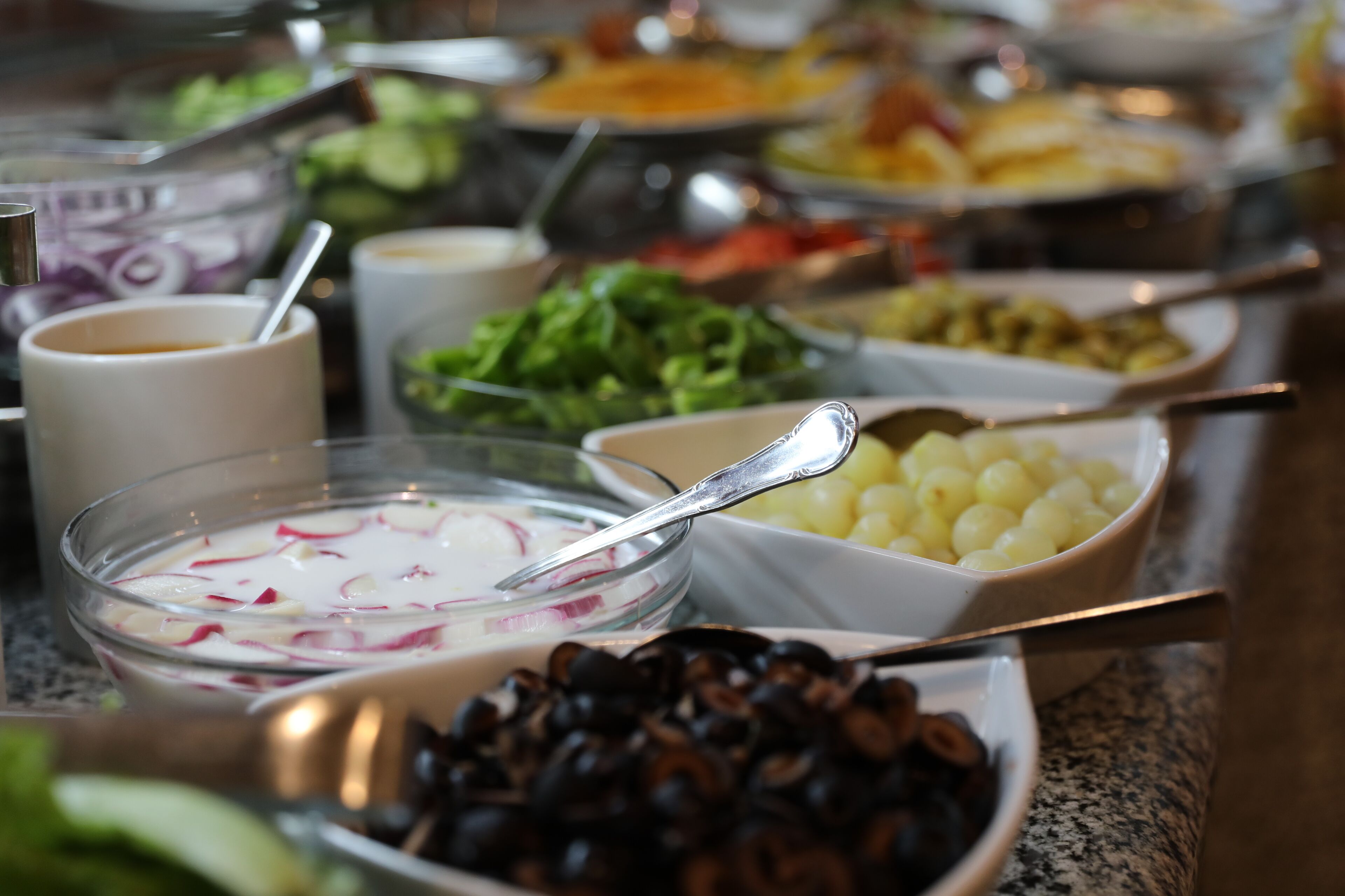 A buffet with various dishes including olives, potatoes, and a salad.