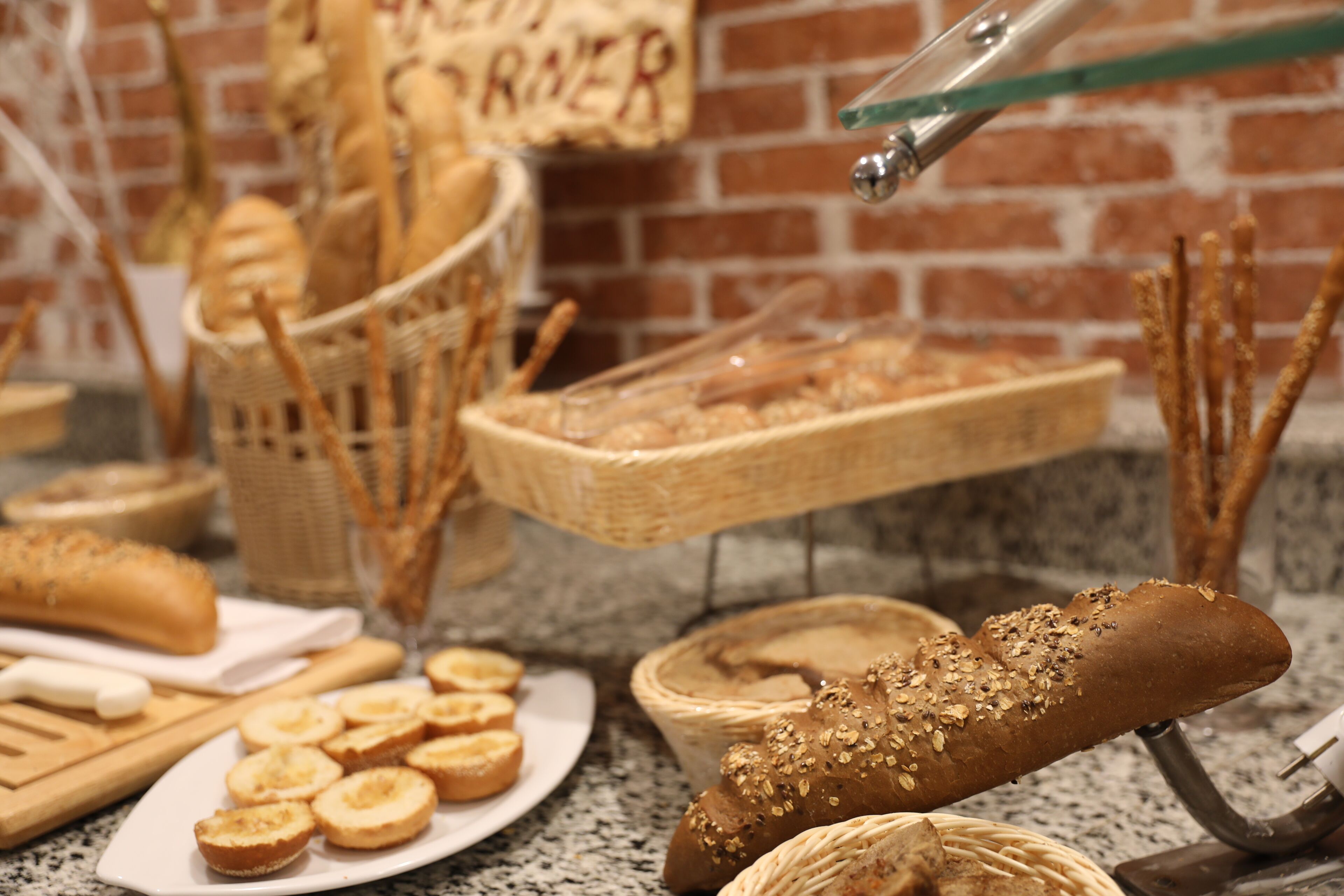 A kitchen counter with various breads and pastries, including a loaf with seeds, and a basket of breadsticks.
