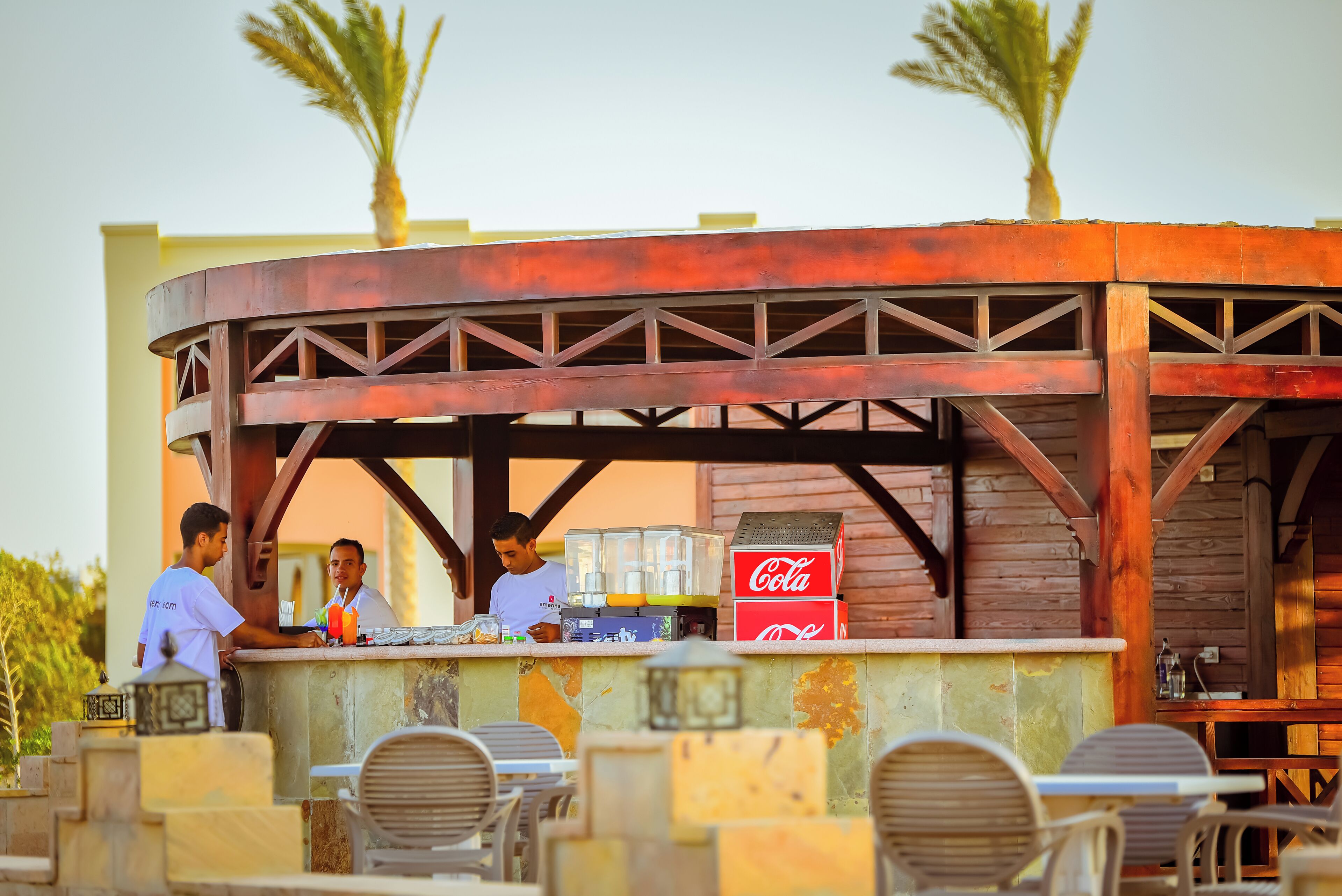An outdoor bar area with wooden structures, seating, and a Coca-Cola cooler.
