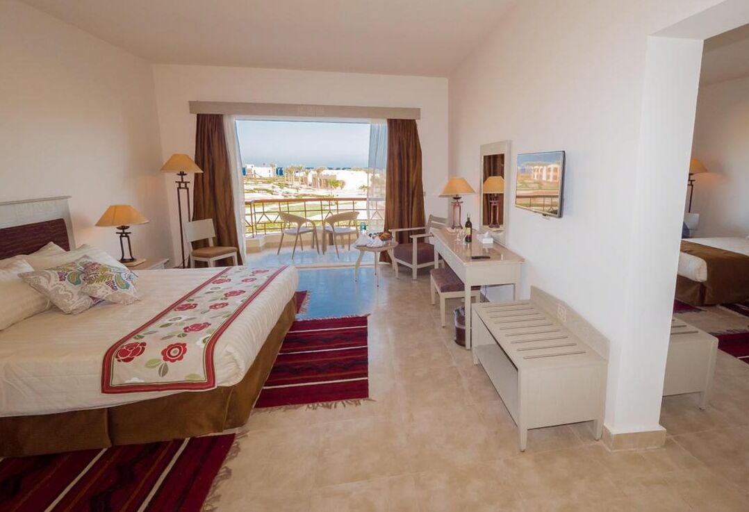 A hotel room with a bed, desk, chair, and a view of the city.
