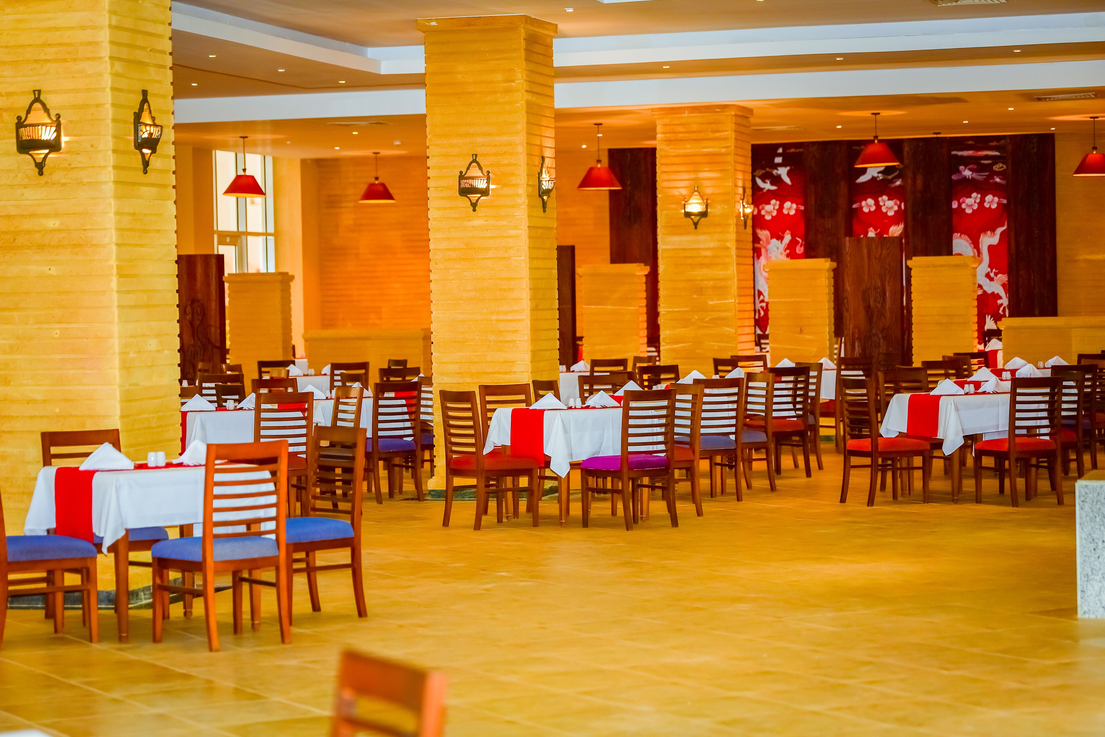 Un comedor amplio con varias mesas y sillas, iluminación cálida y paneles decorativos en las paredes.