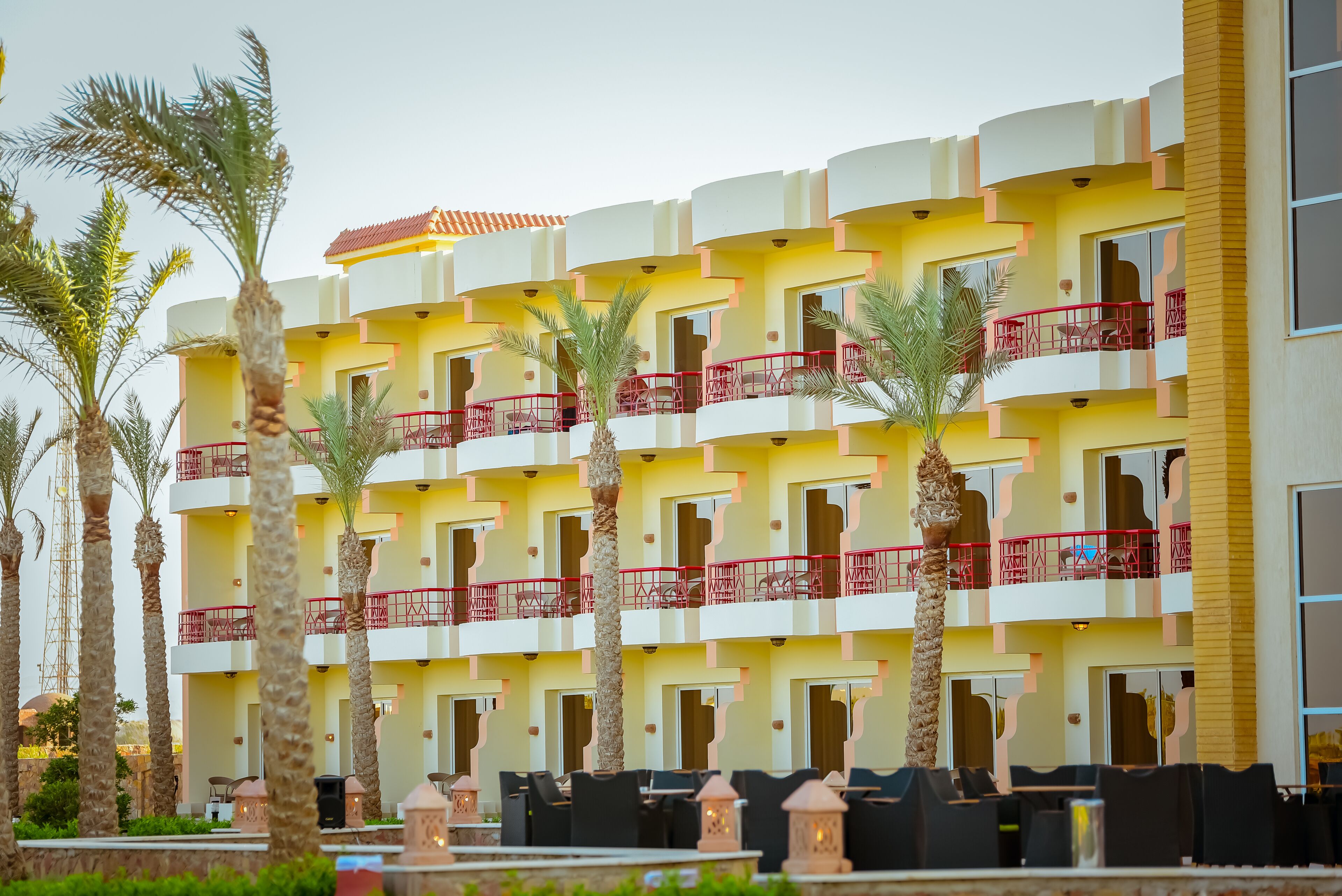 A multi-story hotel with balconies, palm trees, and outdoor seating areas.