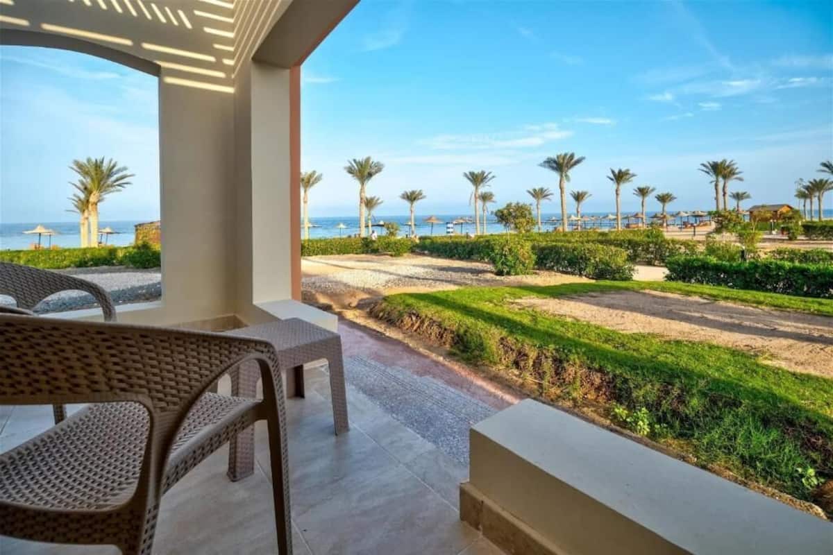Un balcon doté de meubles en osier, offrant une vue sur un jardin aménagé et sur la plage.