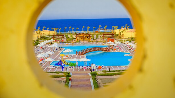 A resort pool area with a view of the ocean, palm trees, and a bridge. - Amarina Queen Resort & Aqua Park Marsa Alam (Marsa Alam)