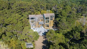 Une maison moderne à deux étages, entourée d’une forêt dense.