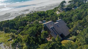 Une propriété située sur la côte, avec une maison entourée d’une forêt dense, offrant une vue sur une plage de sable et l’océan.