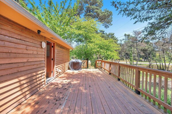 A wooden deck with a covered grill area, a wooden fence, and a building with a door and window.