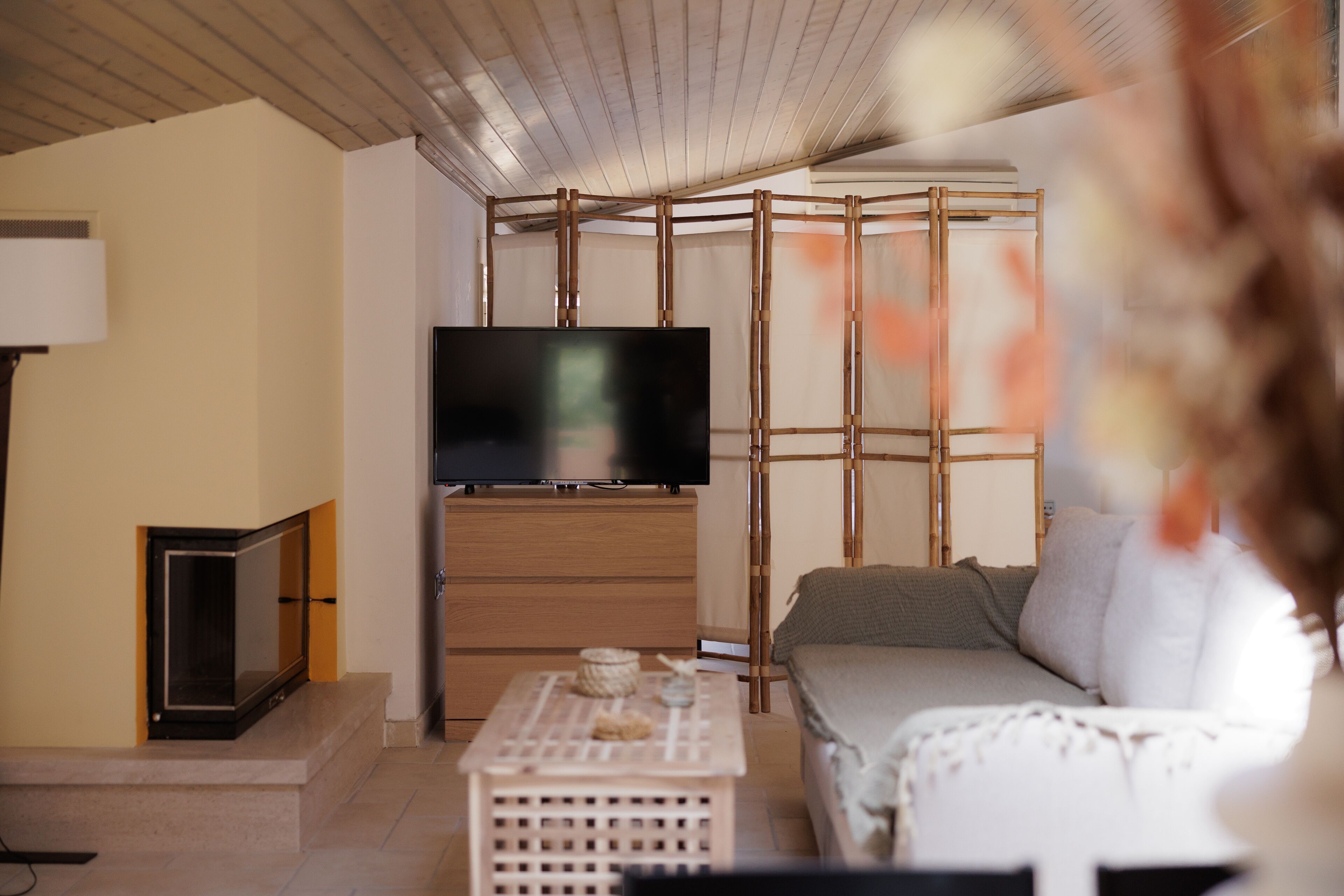 A modern living room with a flat-screen TV mounted on a wooden wall, a sofa, a coffee table, and a lamp.