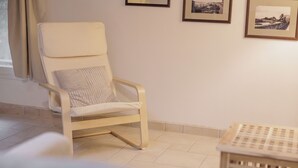 Una habitación con una silla blanca, una mesita pequeña y dos cuadros en la pared.